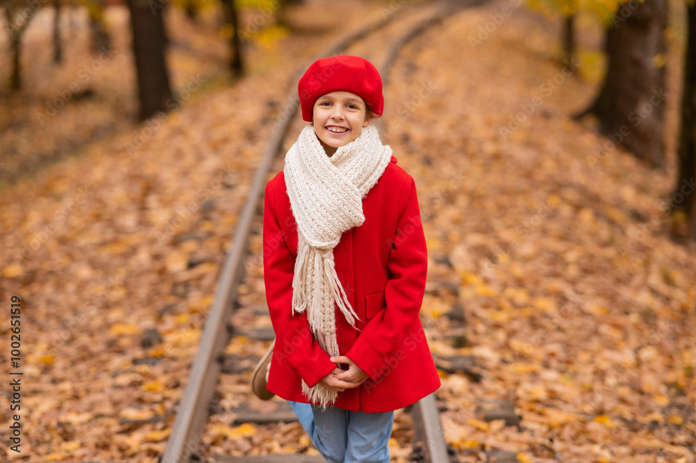 Caucasian girl in a red coat and beret walks along the railway tracks in the park in autumn. Caucasian girl in a red coat and beret walks along the railway tracks in the park in autumn.