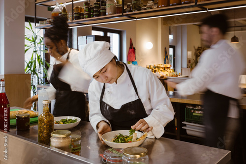 Focused female chef garnishing salad bowl while standing at commercial kitchen at restaurant photo