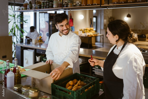 Smiling male chef taking inventory with female colleague in commercial kitchen at restaurant