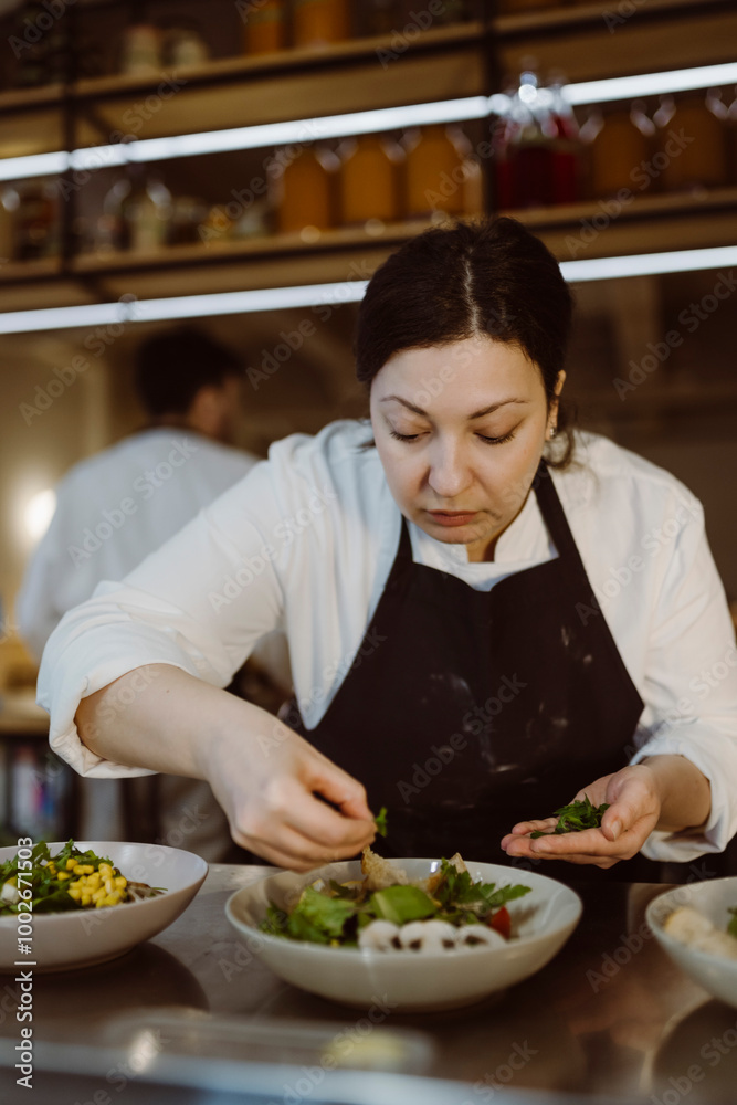 Focused female chef garnishing salad with cilantro in commercial kitchen at restaurant