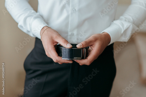 A man is wearing a belt and holding a camera. Concept of professionalism and attention to detail, as the man is dressed in a suit and tie and is focused on his camera