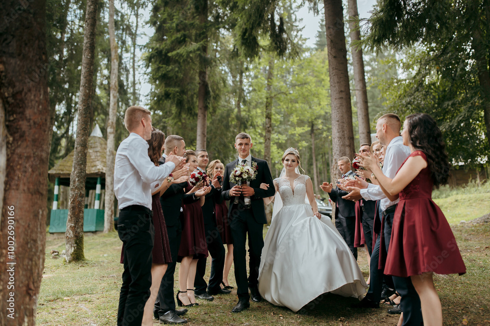 A bride and groom are walking down a path with their wedding party behind them. The bride is wearing a white dress and the groom is wearing a suit. The wedding party is dressed in black and red A bride and groom are walking down a path with their wedding party behind them. The bride is wearing a white dress and the groom is wearing a suit. The wedding party is dressed in black and red