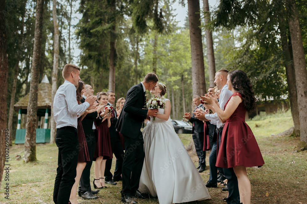 Obraz premium A bride and groom are surrounded by their wedding party, with the bride and groom kissing each other