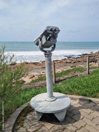 Public telescope overlooking the ocean with a rocky shoreline and greenery