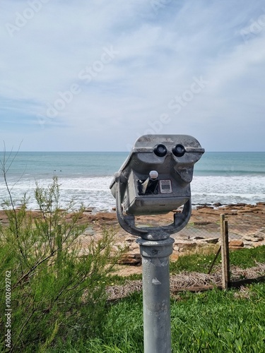 Public telescope facing the ocean with a rocky shoreline in the background