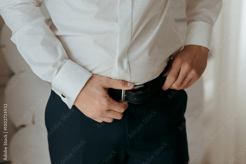 A man in a white shirt and blue pants is adjusting his belt. Concept of formality and attention to detail, as the man takes care to ensure his outfit is properly fitted A man in a white shirt and blue pants is adjusting his belt. Concept of formality and attention to detail, as the man takes care to ensure his outfit is properly fitted