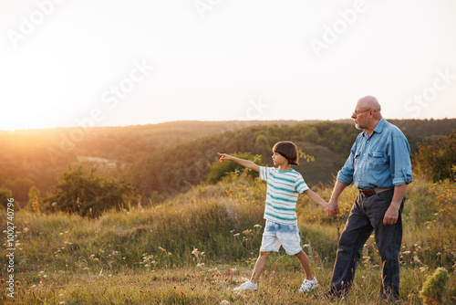 Photo of a little boy with his grandfather walking in a field at summer