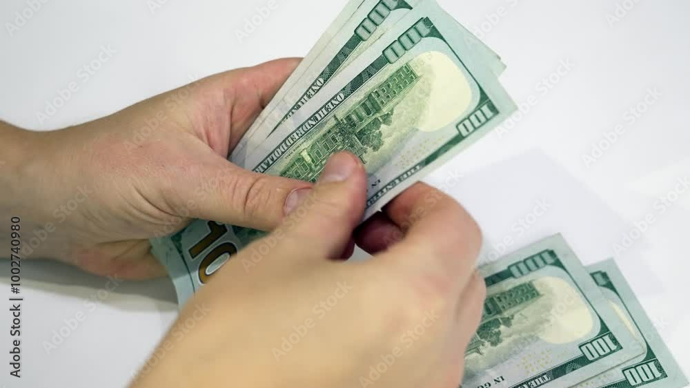 A person is counting several hundred dollar bills, meticulously organizing the cash on a clean surface. The setting is relaxed, allowing for a clear focus on the currency.