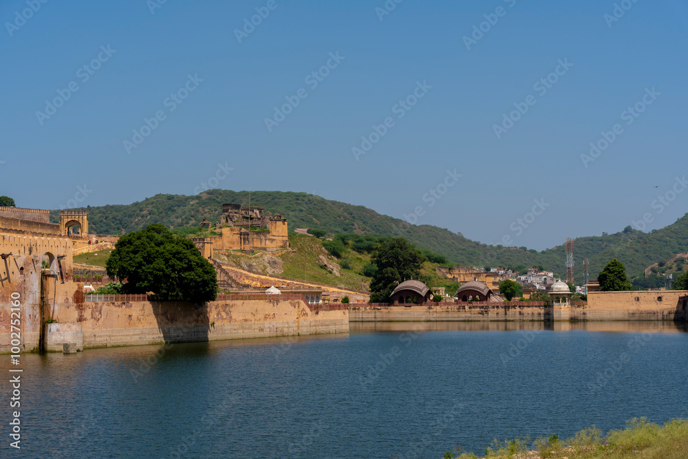 Fototapeta premium the majestic Amber Fort in Jaipur, Rajasthan, overlooking Maota Lake. The fort’s golden-yellow sandstone facade stands out against the lush greenery and clear blue sky.