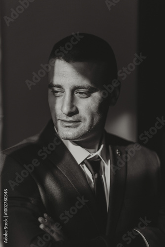 A man in a suit and tie is standing in front of a wall. He is looking at the camera with a serious expression