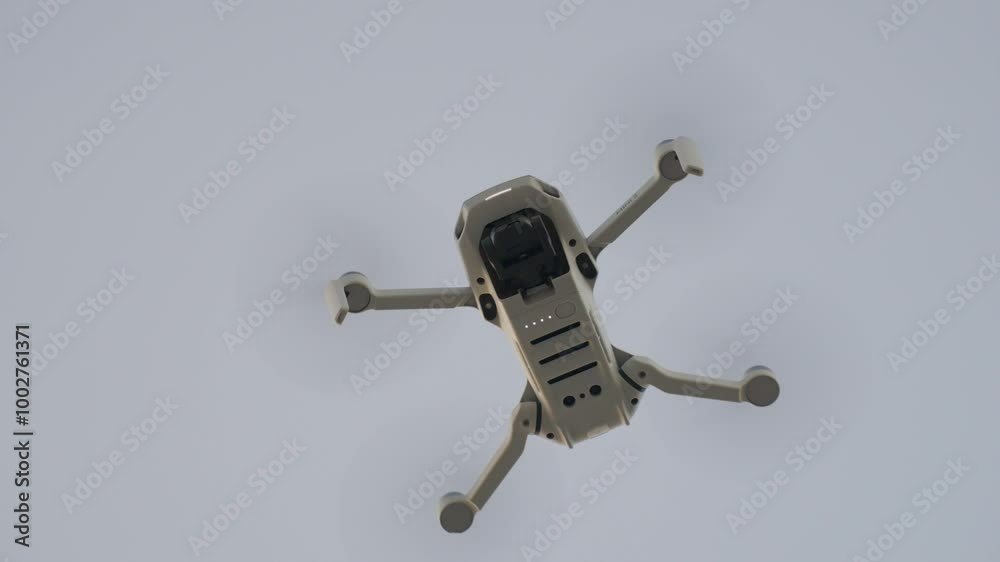 Drone flying high in the sky during daytime, showing its underside Drone flying high in the sky during daytime, showing its underside