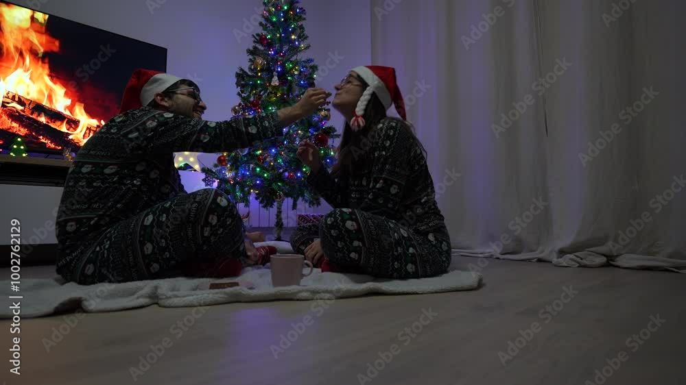 Young couple with Christmas sweaters and Santa´s hats eating some chocolate at home Young couple with Christmas sweaters and Santa´s hats eating some chocolate at home