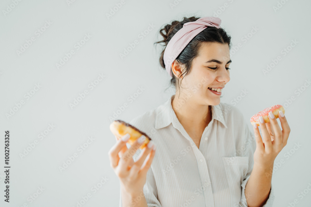 Young caucasian woman eating and posing with donuts on white wall Young caucasian woman eating and posing with donuts on white wall