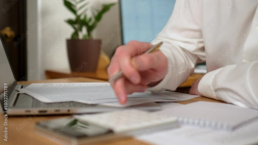Man Sitting at Desk in Office Diligently writing on Piece of Paper, Calculates Costs and Revenues on Calculator, close up. Male Freelancer working from home. Browsing internet, using social networks Man Sitting at Desk in Office Diligently writing on Piece of Paper, Calculates Costs and Revenues on Calculator, close up. Male Freelancer working from home. Browsing internet, using social networks