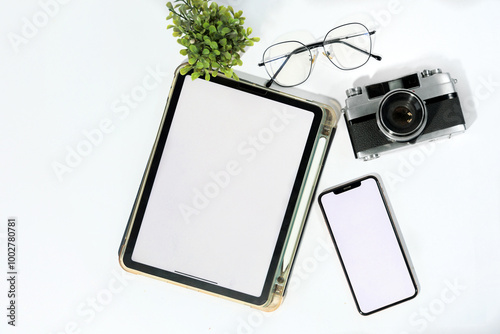 A tablet and a cell phone sit on a table next to a camera