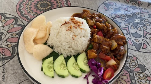 Top angle view of white rice with chicken black pepper served with cucumber slices and crackers. Indonesian food called Ayam Lada Hitam