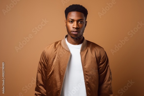 Portrait of a satisfied afro-american man in his 20s wearing a trendy bomber jacket isolated on light wood minimalistic setup