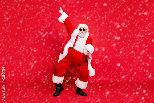 Full size photo of funny fat overweight santa claus with big abdomen in eyewear dance raise hand wear style stylish trendy trousers pants isolated over red background