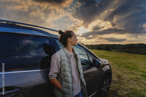 Obraz na płótnie Young female driver standing by car enjoying sunset and nature in field during road trip w salonie