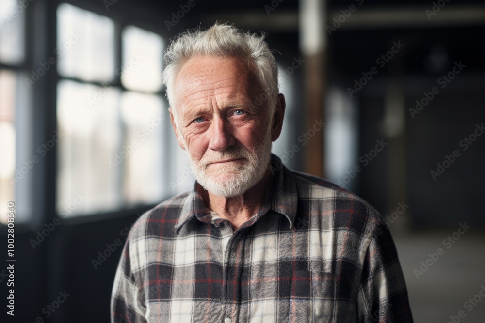 Portrait of a tender man in his 70s dressed in a relaxed flannel shirt on empty modern loft background Portrait of a tender man in his 70s dressed in a relaxed flannel shirt on empty modern loft background