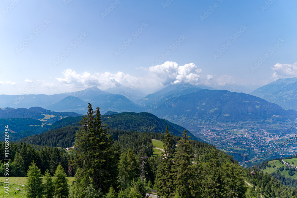 Obraz premium Aerial view of Italian City of Meran with Etsch Valley and Etsch River seen from mountain resort Meran 2000 on a sunny summer day. Photo taken July 18th, 2024, Meran Merano, Italy.