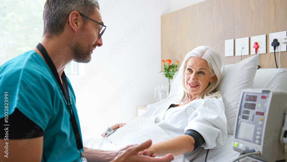 Obraz premium Male Nurse Taking Mature Female Patients Blood Pressure In Hospital Bed With Automated Machine