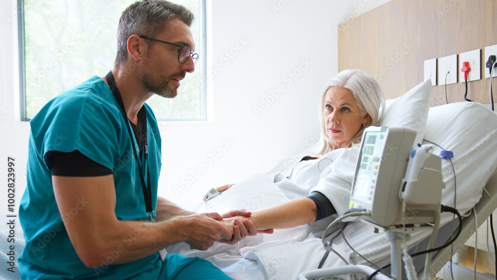 Obraz premium Male Nurse Taking Mature Female Patients Blood Pressure In Hospital Bed With Automated Machine