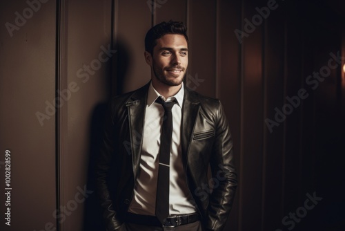 Portrait of a cheerful man in his 20s sporting a stylish leather blazer isolated in bare monochromatic room