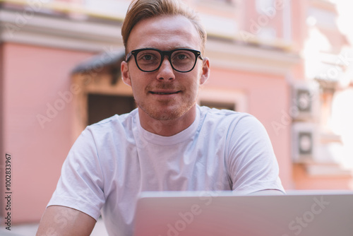 Portrait of skilled male IT professional in stylish eyewear looking at camera during break from online programming and initializing data system, successful man spending time for creating article photo