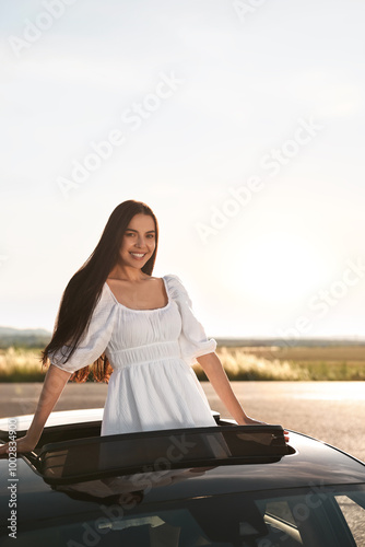 Enjoying trip. Smiling woman leaning out of car roof outdoors