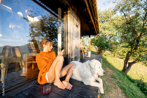 Wallpaper Mural Woman in an orange sweater relaxing with her dog on a wooden deck during sunset, browsing her phone. Calm evening light, surrounded by nature Torontodigital.ca