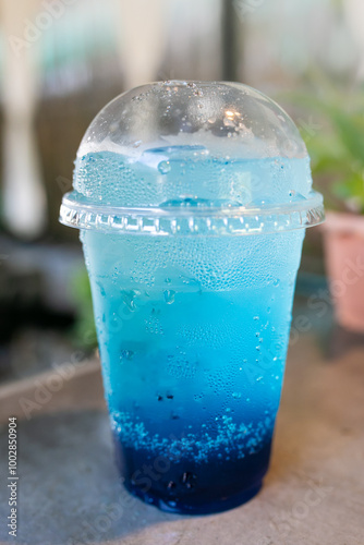 Blue soda drink in plastic cup on wooden table with blurred background.