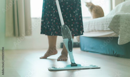 Obraz na płótnie A woman is cleaning the floor with a mop. A cat is sitting on the bed w salonie