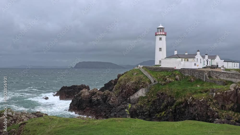 Fanad Head Lighthouse stands on a rugged coastline in Ireland, surrounded by the Atlantic Ocean under overcast skies, with rough seas hitting the rocky shore Fanad Head Lighthouse stands on a rugged coastline in Ireland, surrounded by the Atlantic Ocean under overcast skies, with rough seas hitting the rocky shore