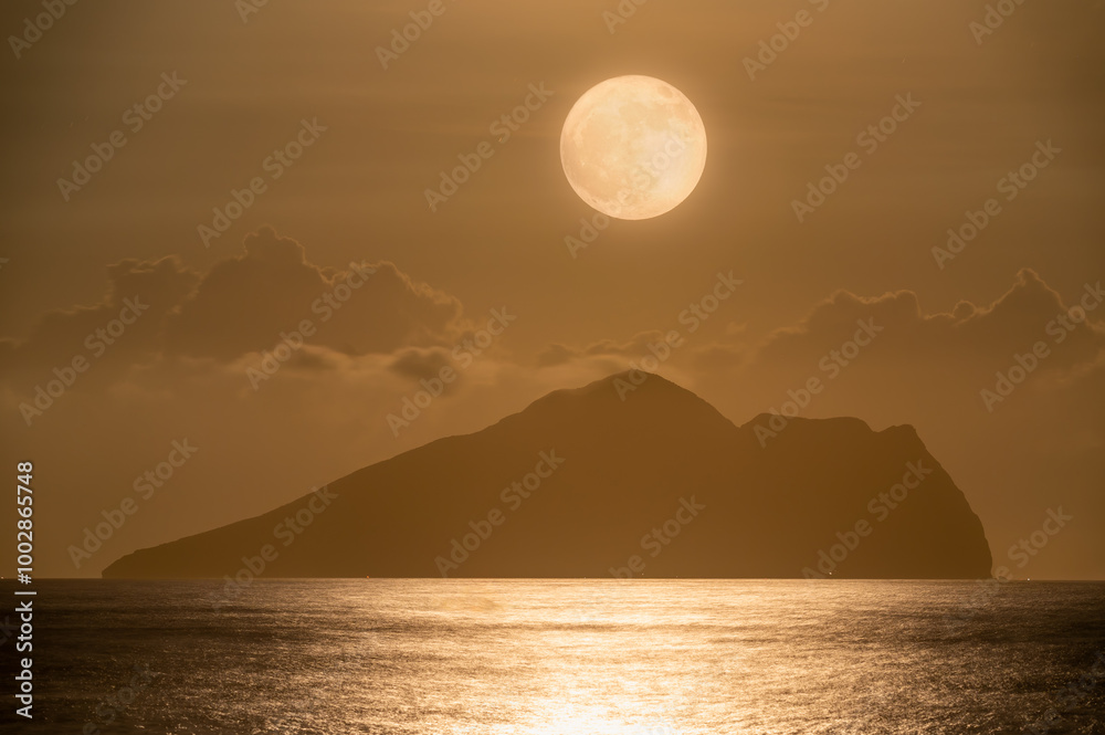 A serene night scene of the ocean with gentle waves, featuring a mesmerizing moonrise behind the iconic Turtle Island, Yilan, Taiwan. The moon gracefully dances through the clouds. A serene night scene of the ocean with gentle waves, featuring a mesmerizing moonrise behind the iconic Turtle Island, Yilan, Taiwan. The moon gracefully dances through the clouds.