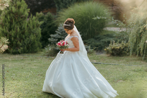 A young woman in a white dress is walking through a garden, holding a bouquet of flowers