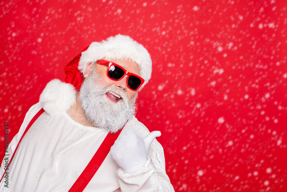 Close up photo of cheerful funny fat overweight style stylish trendy santa claus in eyewear pointing at copyspace recommend winter season sales isolated over red background