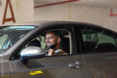 Young businessman putting a seatbelt on. Ready to drive off from his parking spot in an underground garage.