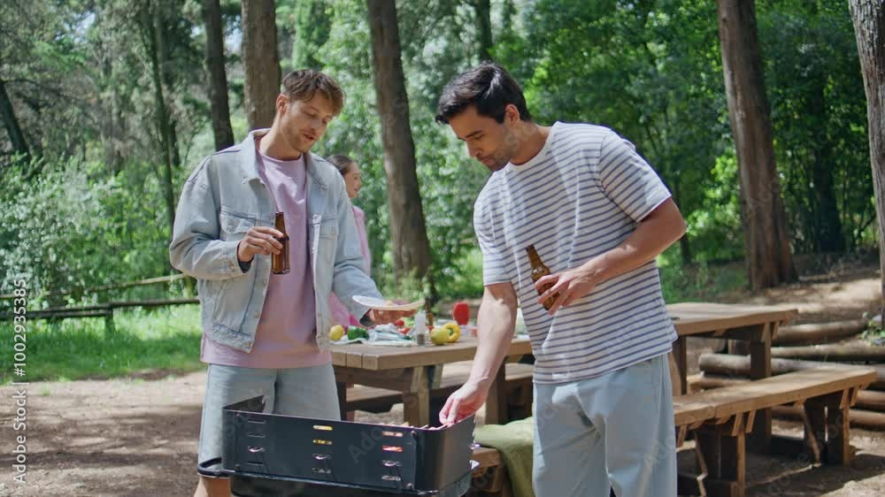 Two men grilling food holding beer at summer forest barbecue closeup. Friends