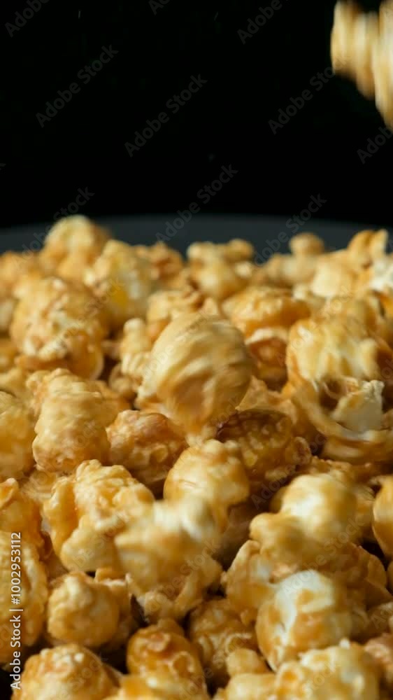 Caramelized sweet popcorn pours and spins, black background, vertical slow motion Caramelized sweet popcorn pours and spins, black background, vertical slow motion