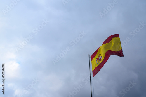 Bandera de España ondeando al viento en mástil sobre cielo nublado