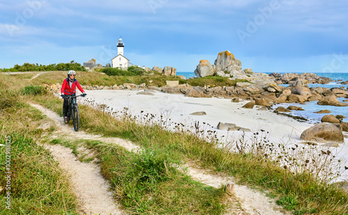 nice senior woman cycling with her electric mountain bike at the rocky rose granite coast at Meneham site in Brittany, France next to Kerouarn