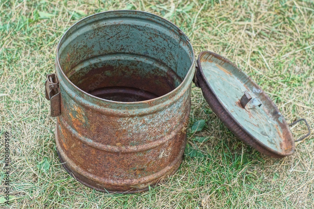 Fototapeta premium one round rusty retro iron dirty empty open old with lid industrial with handle and latches large container stands on green day outside 