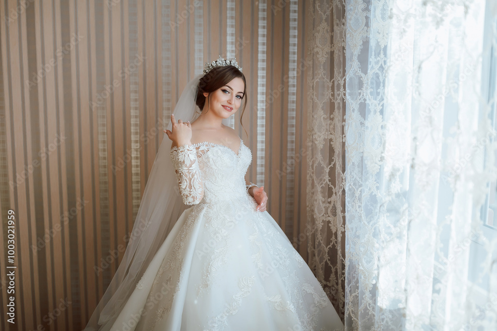 A woman in a wedding dress is standing in front of a window. She is wearing a veil and a tiara A woman in a wedding dress is standing in front of a window. She is wearing a veil and a tiara