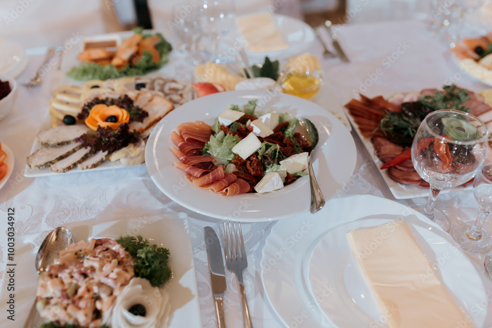 A table with a variety of food and drinks, including a salad, meat, and cheese. The table is set with utensils and glasses, and there are several bottles and cups on the table A table with a variety of food and drinks, including a salad, meat, and cheese. The table is set with utensils and glasses, and there are several bottles and cups on the table
