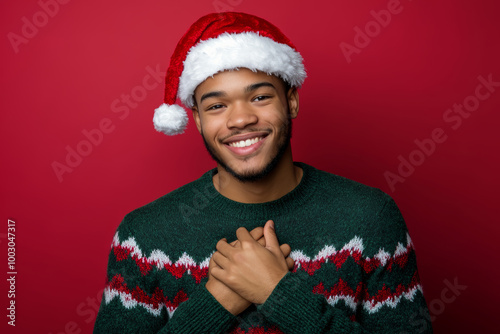 A cheerful young man in a Santa hat and Christmas sweater expresses joy and warmth, embodying holiday spirit in a vibrant setting photo