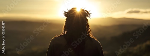 Jesus Christ with a crown of thorns on his head, seen from behind, looking at the sun in a mountainous landscape