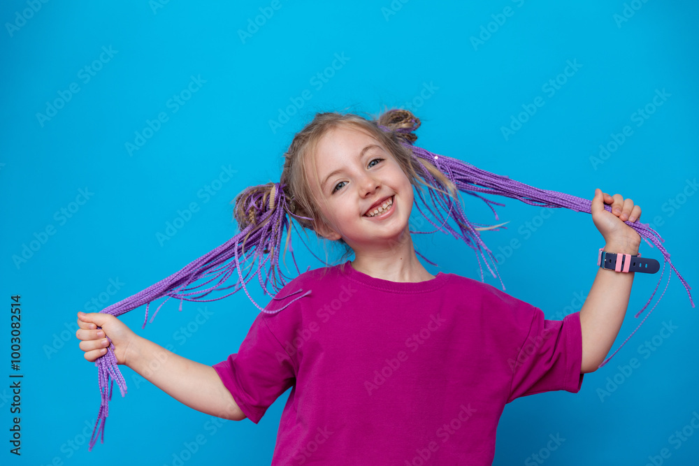 Portrait of happy laughing beautiful little girl with purple braided afro-pigtails dreadlocks. A child in a bright pink t-shirt on a blue background. Fashionable, stylish, bright hairstyle. Copy space Portrait of happy laughing beautiful little girl with purple braided afro-pigtails dreadlocks. A child in a bright pink t-shirt on a blue background. Fashionable, stylish, bright hairstyle. Copy space