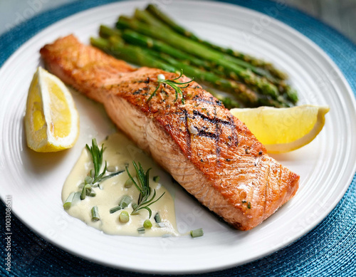 A beautifully plated seafood dish featuring grilled salmon, asparagus, and lemon wedges. The