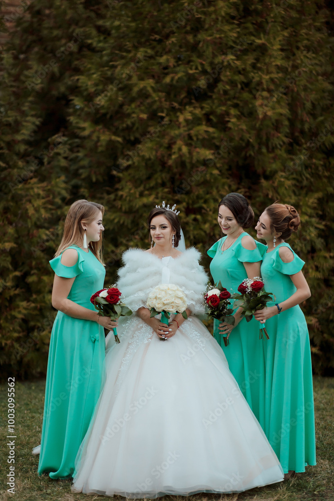 Fototapeta premium A bride and her bridesmaids pose for a picture. The bride is wearing a white dress and a green jacket